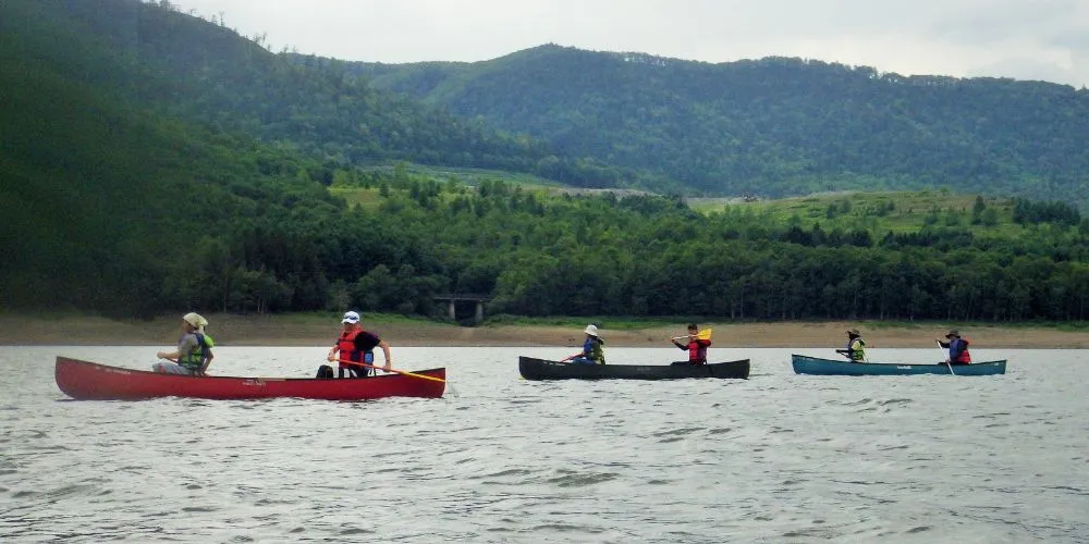 A fleet of three Canadian canoes paddling in a line across the vast and scenic Lake Kanayama.
