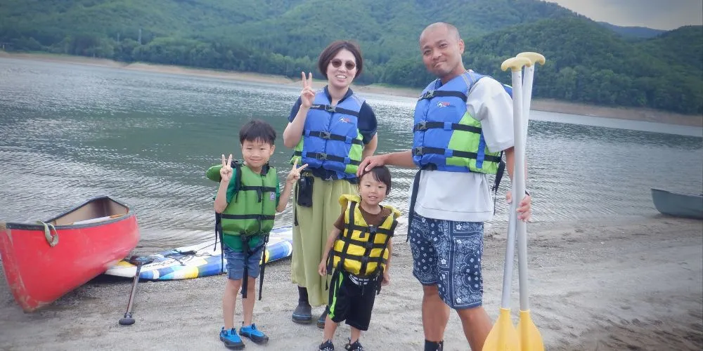 A happy family of four posing on the shore after their enjoyable Canadian canoe tour.