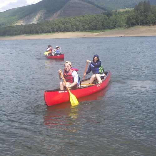 Two canoes with four people paddling together on the open water of the lake.