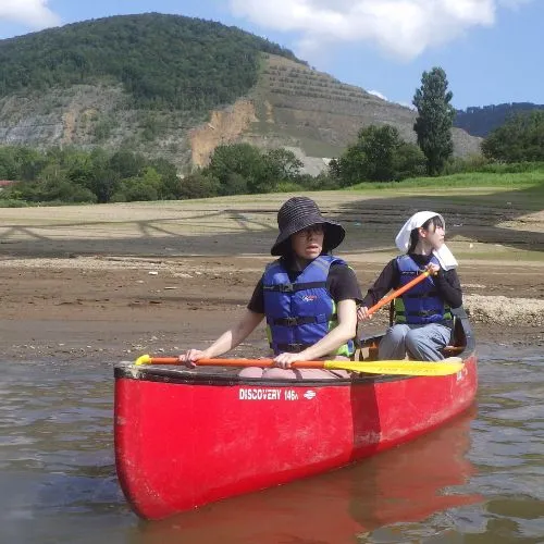 A close-up shot of two participants paddling a red Canadian canoe near the shore.