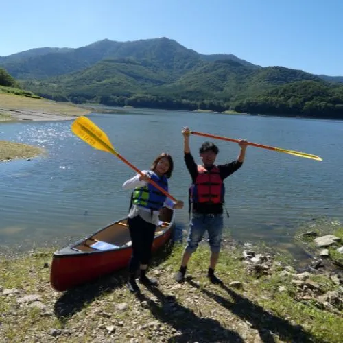 A couple posing triumphantly with their paddles next to their canoe on the shore.