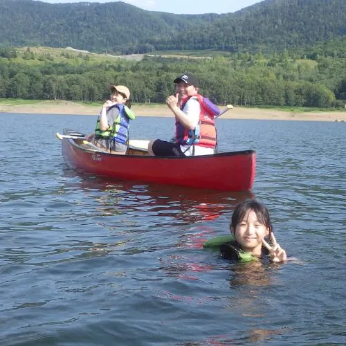 Children laughing and swimming in the lake next to their Canadian canoe on a warm day.