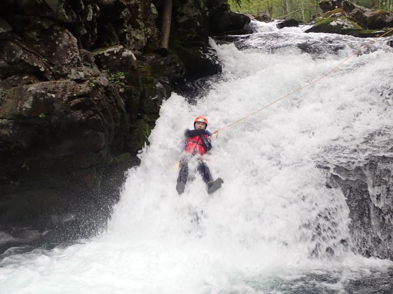 An adventurer abseiling down a powerful waterfall, showcasing the thrilling and technical aspects of the Wild Canyoning course.