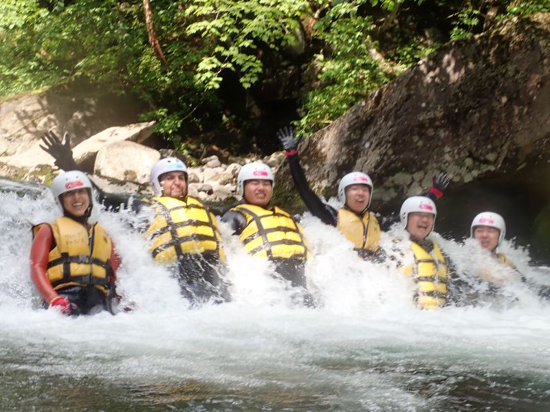 A group of excited rafters waving from within the intense whitewater of a waterfall pool on the Wild Canyoning tour.