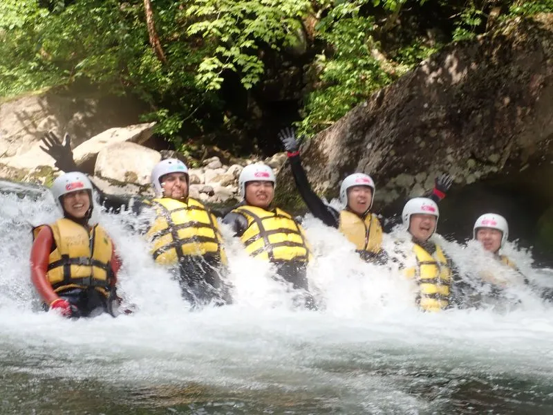A group of excited rafters waving from within the intense whitewater of a waterfall pool on the Wild Canyoning tour.
