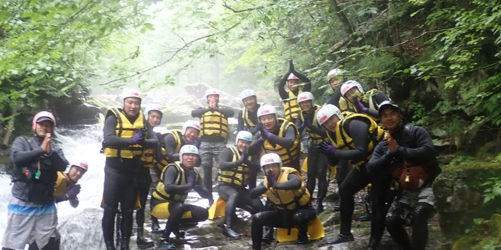 A large group of adventurers posing playfully in front of a waterfall, celebrating their completion of the Wild Canyoning tour.