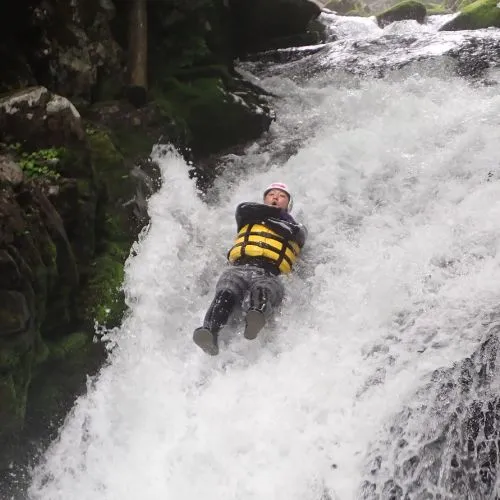 A participant sliding down a fast-flowing natural waterslide with a huge splash.