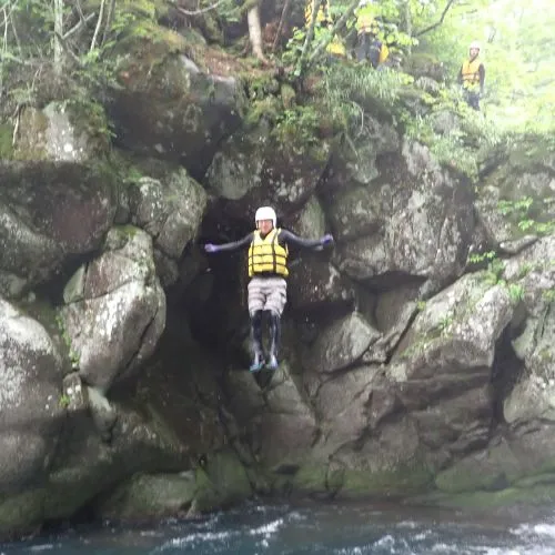 An adventurer captured mid-air, taking a thrilling leap from a high rock into the deep pool below.
