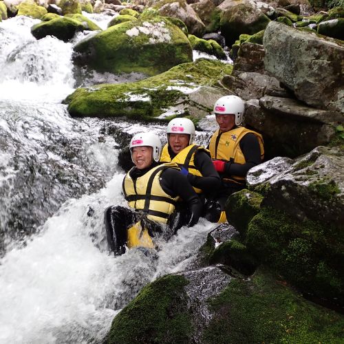 A group of three adventurers sitting together in a powerful waterfall, like a natural spa.