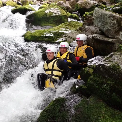 A group of three adventurers sitting together in a powerful waterfall, like a natural spa.