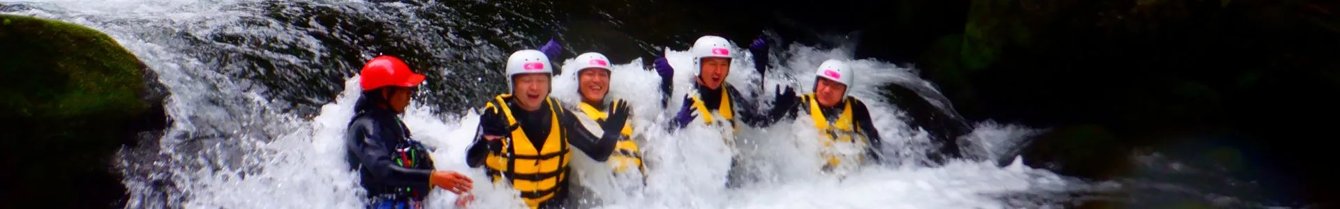 A group of adventurers laughing and waving amidst the powerful whitewater of a waterfall, showcasing the thrill of the Wild Canyoning tour.