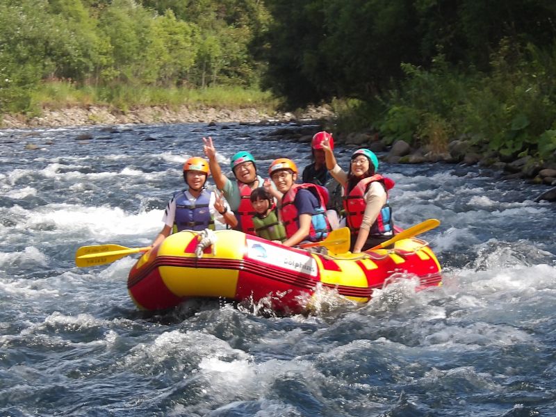A happy family, including a young child, waving and smiling while enjoying a fun and safe rafting adventure on the Chubetsu River.