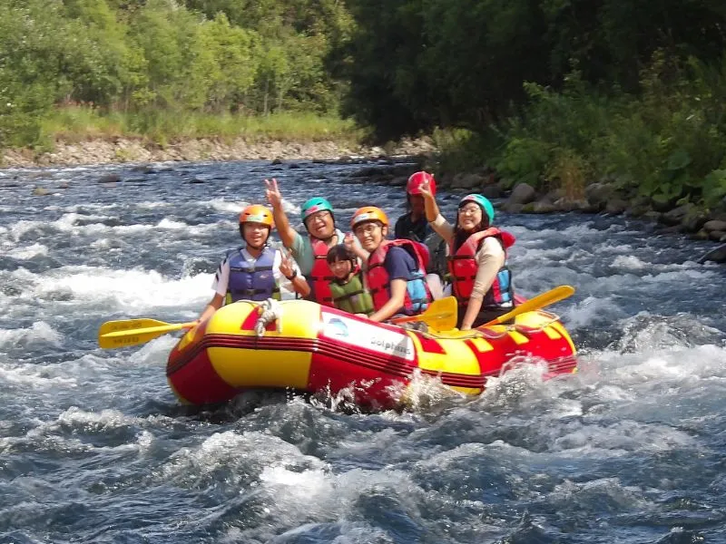 A happy family, including a young child, waving and smiling while enjoying a fun and safe rafting adventure on the Chubetsu River.