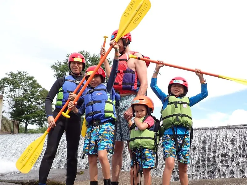 A family posing with their paddles held high in front of a scenic waterfall, a memorable photo spot on the Chubetsu River tour.