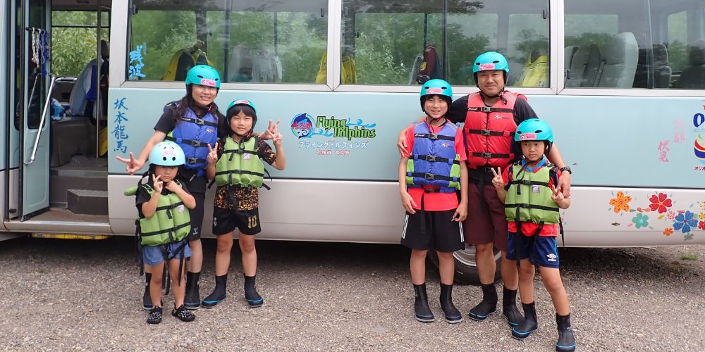 A family posing for a photo in front of the Flying Dolphins tour bus, fully geared up and ready for their rafting adventure.