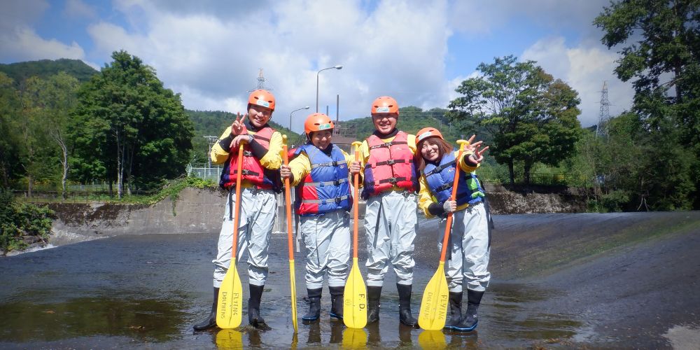 A group of four smiling rafters posing with their paddles in a calm section of the Chubetsu River after the main rapids.
