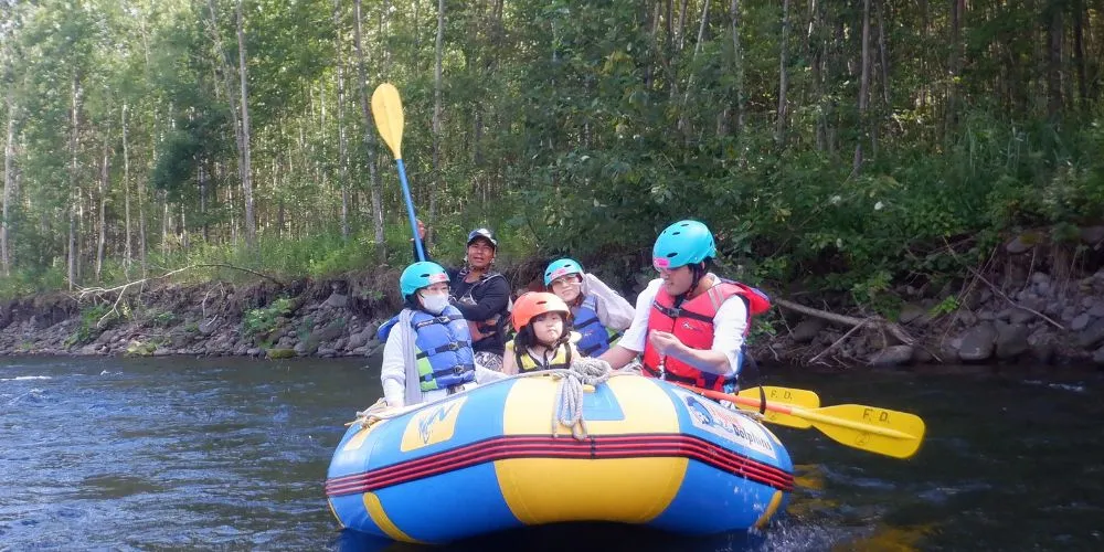 A family enjoying a gentle rafting tour on the Chubetsu River, with a guide steering the boat from the back.