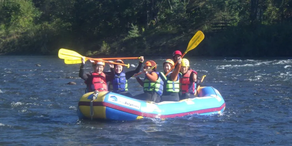 A cheerful group of rafters raising their paddles in excitement while navigating a fun section of the Chubetsu River.