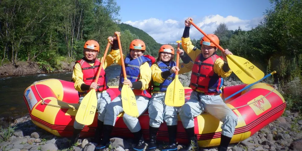 A team of four rafters posing with their paddles on the scenic bank of the Chubetsu River, celebrating the end of their tour.