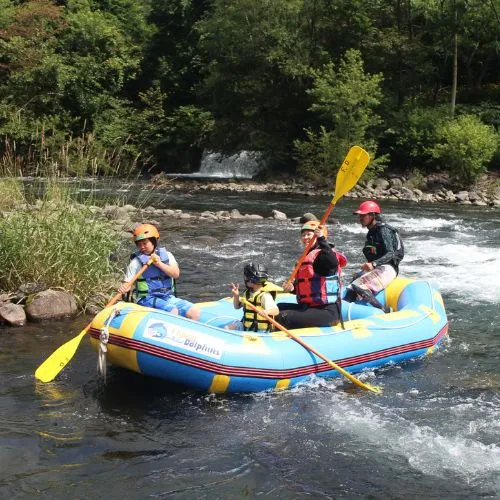 A family with young children paddling together in a raft on a calm section of the river, surrounded by lush greenery.