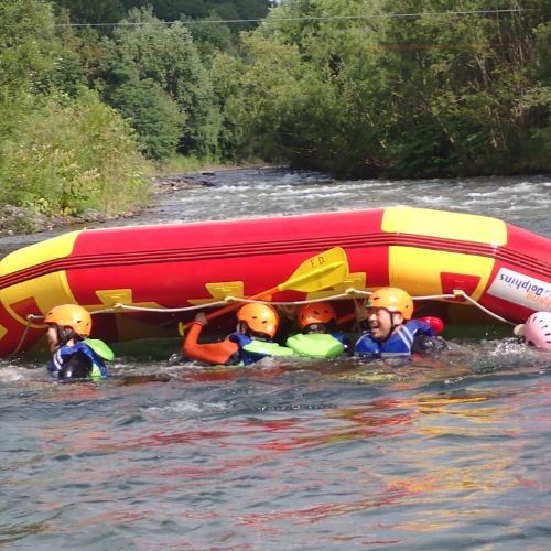 Children smiling and swimming around an overturned raft, learning water safety in a playful way.