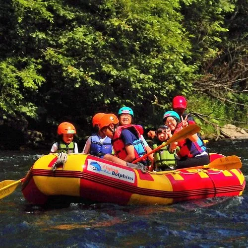 A family of five waving happily from their raft as they navigate the river on a sunny day.