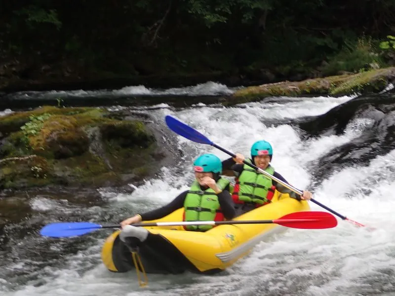 A smiling couple posing in their ducky in front of a beautiful, cascading waterfall on the river.