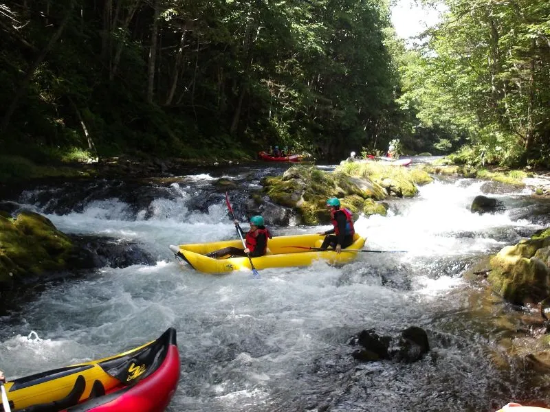 Two friends laughing and working together to paddle their inflatable kayak through the river's current.