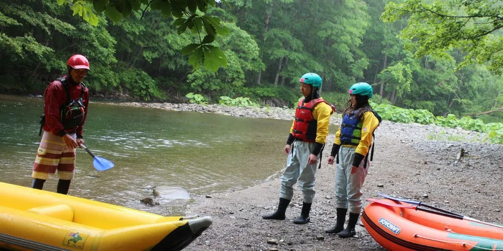 A guide giving a hands-on paddling lesson to two participants on the riverbank before starting the tour.