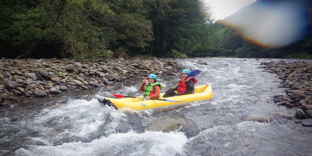 A parent and child paddling their ducky together on a calm, scenic stretch of the river.