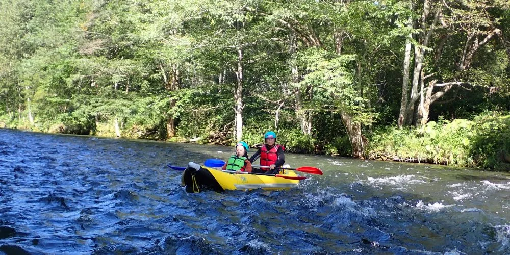 A couple giving peace signs while skillfully navigating their ducky through exciting whitewater.