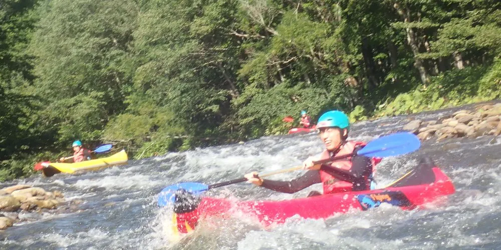 An adventurer paddling solo in a red ducky, creating a large splash as they navigate the rapids.