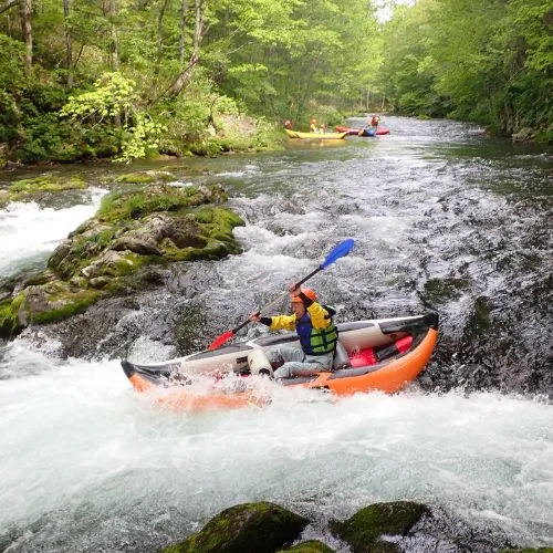 A person in a ducky paddling through a rapid, creating a large splash.