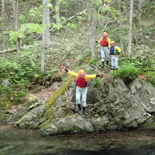 A person jumping from a small cliff into the river next to their ducky.