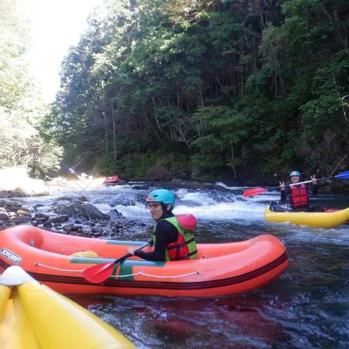 A line of several duckies with participants paddling down a calm section of the river.