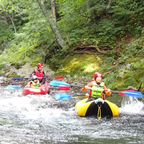 Two people in a tandem ducky paddling in sync on a calm section of the river.