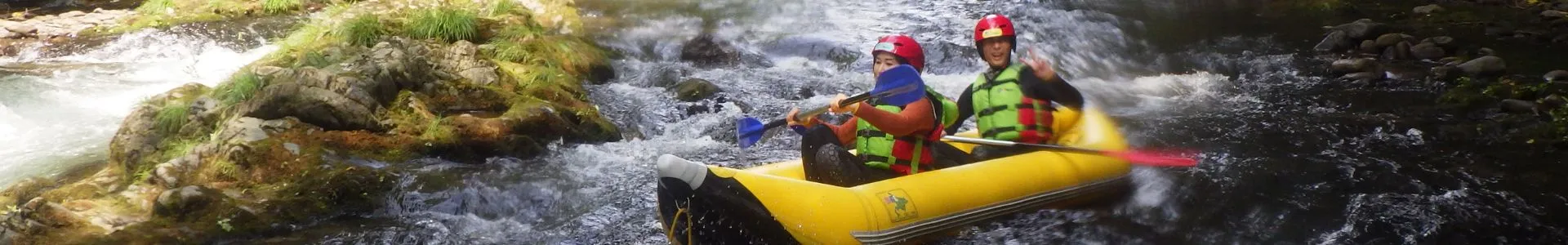 Two participants joyfully paddling a two-person inflatable kayak (Ducky) through exciting river rapids.