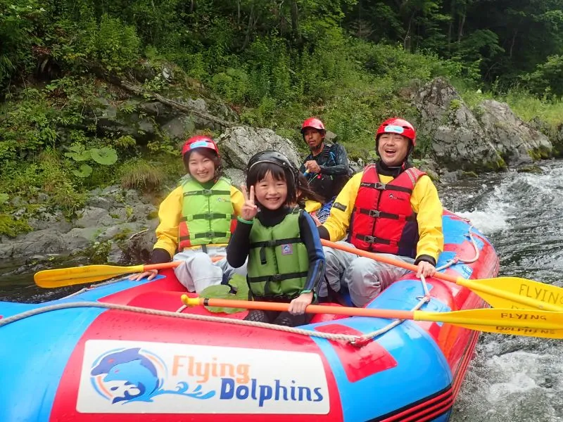 A family smiling together on a raft, with a young girl in the front giving a peace sign, suitable for all ages.
