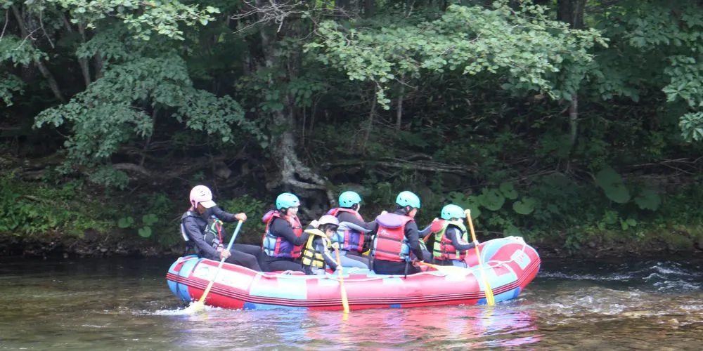 A family rafting boat gliding along a calm, tree-lined section of the river, perfect for a relaxing adventure.