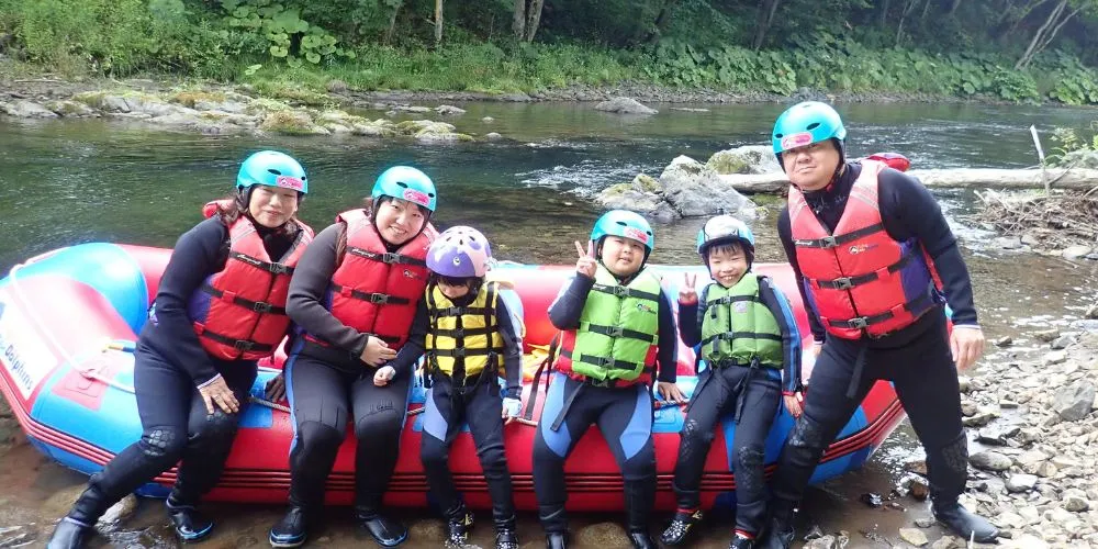 A happy family posing for a memorable group photo by their raft on the riverbank after a fun-filled tour.