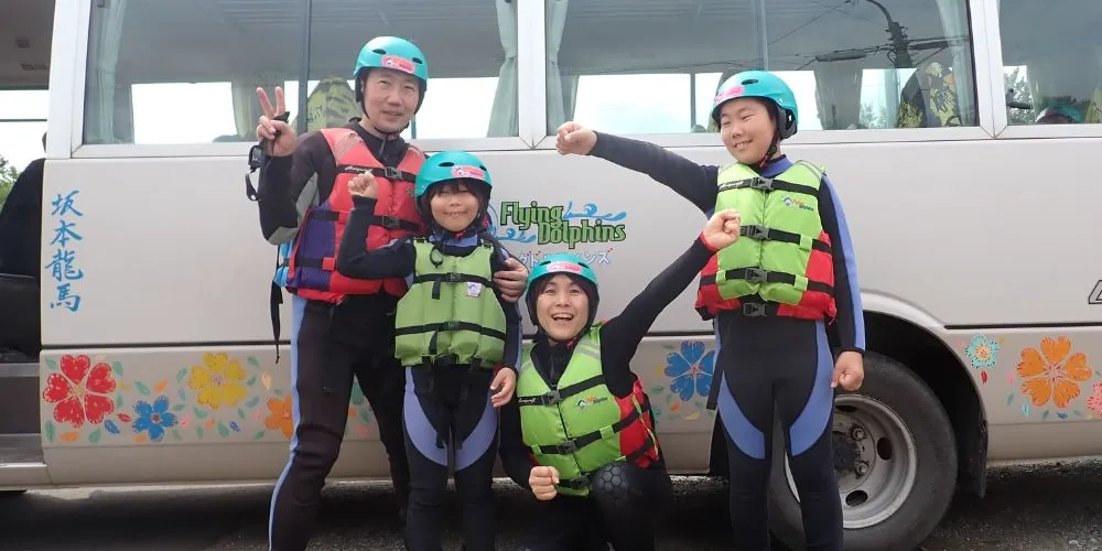 A family in full rafting gear, posing excitedly in front of the Flying Dolphins transfer bus.