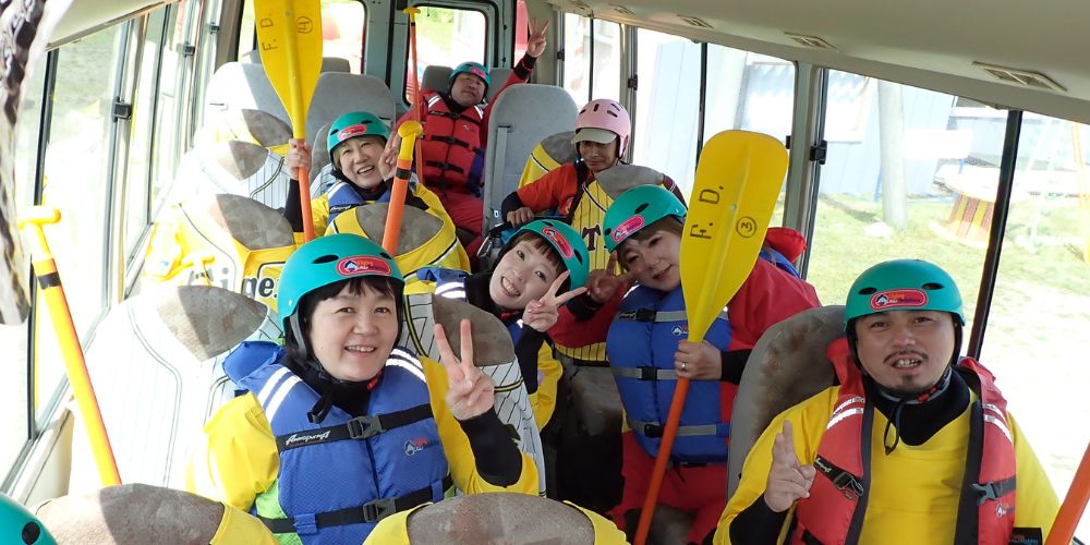A happy group of participants in full rafting gear, smiling and ready for adventure inside the transfer bus.