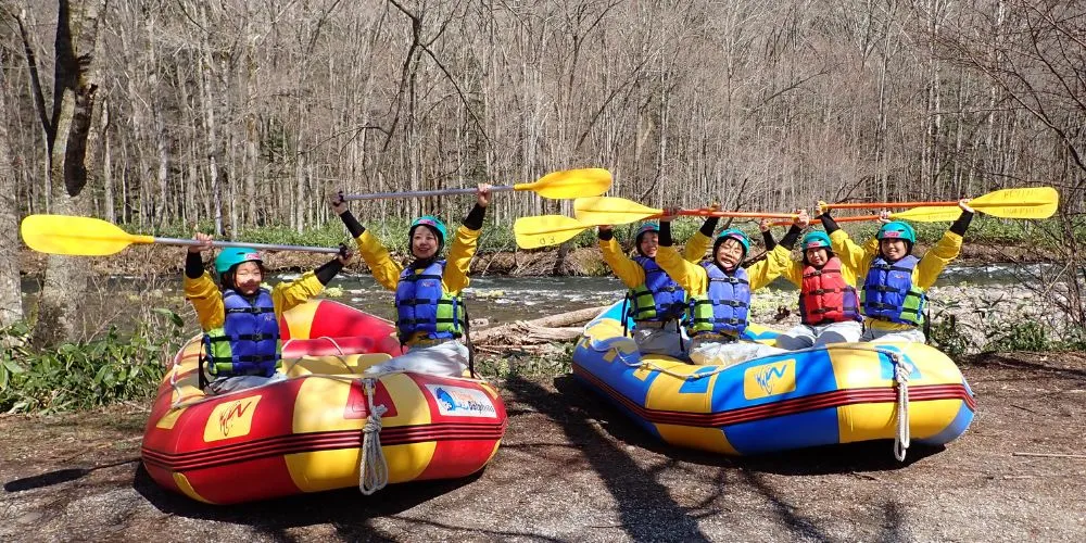A team of rafters fully equipped, posing with their paddles up before starting the tour.
