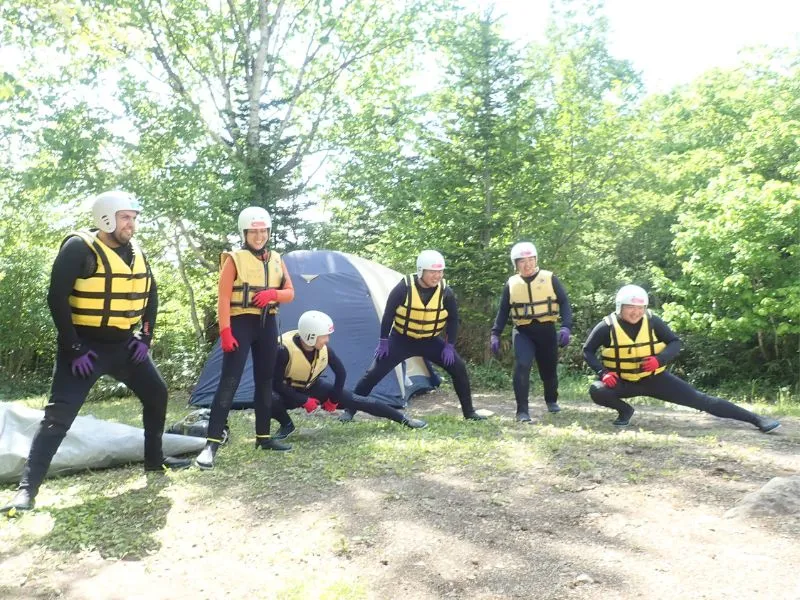 A group of participants led by a guide doing warm-up stretches before a canyoning tour, demonstrating the focus on safety preparation.