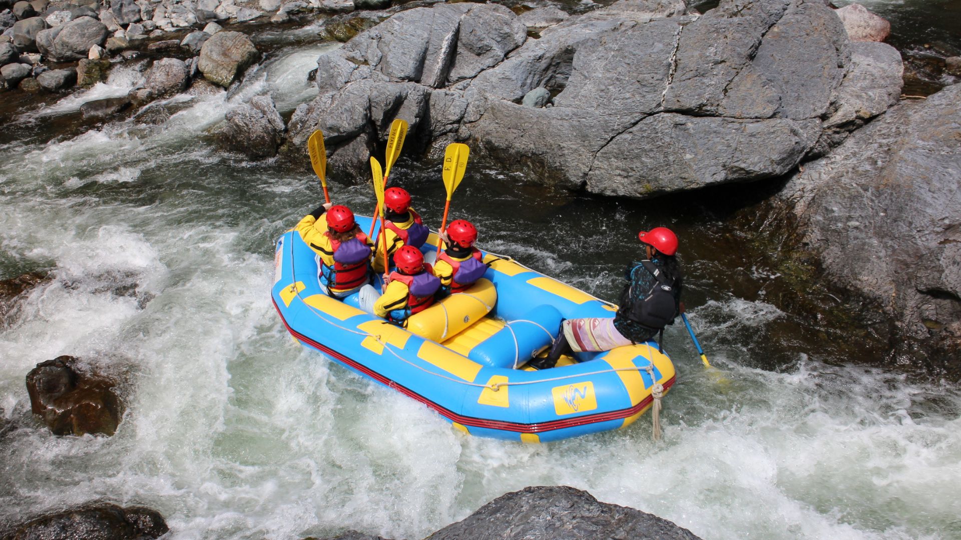 Three happy participants waving from a raft on a calm stretch of the river, surrounded by lush green forest scenery in Hokkaido.