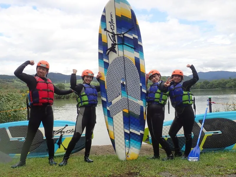A group of four smiling participants posing energetically with their SUP board on the shore after a fun and successful tour.
