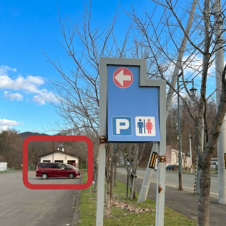A road sign pointing left to the parking area and restrooms, seen when approaching from the Furano side.