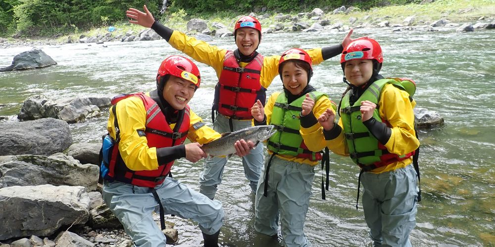 A joyful group of four participants posing with a large fish caught from the river, celebrating their successful adventure.