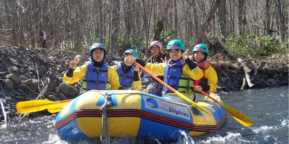 A group of four participants actively paddling and navigating rapids on the Sorachi River.