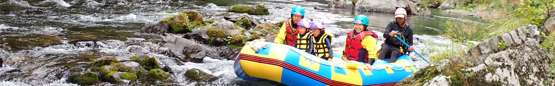 A family with two children enjoying a family rafting tour, navigating through gentle rapids surrounded by the lush green nature of Furano.